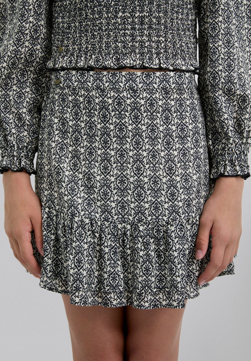 Falda con estampado en blanco y negro y dobladillo con volantes, hecha de tejido texturizado. Presenta una cinturilla con fruncido y botones decorativos.