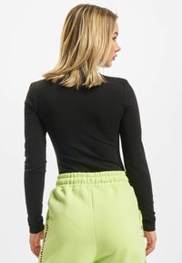 Svart langermet topp kombinert med lysegrønne joggebukser med elastisk midje og sidelommer. Glatt stoffstruktur.