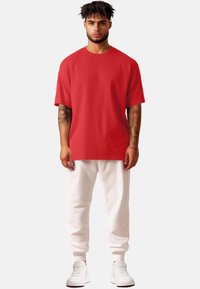 T-shirt rossa a maniche corte con una vestibilità ampia, abbinata a pantaloni della tuta bianchi e sneakers bianche. Il tessuto sembra liscio e leggero.