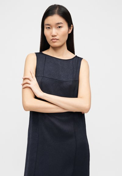 Varrukateta tumesinine kleit tekstuurse kangaga, ümmarguse kaeluse ja sirge siluetiga. Modell seisab käed rüpes, näidates rõiva disaini.