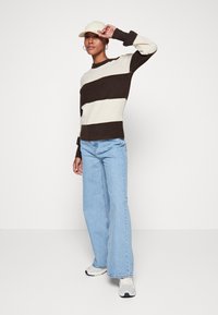 Pull en tricot avec des rayures horizontales crème et marron, col rond et poignets côtelés, associé à un jean large bleu clair et des baskets.