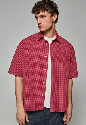 Short-sleeve red button-up shirt with a white grid pattern, made of lightweight fabric, featuring a pointed collar and front button closure.