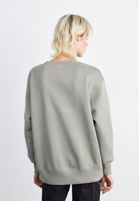 Sweatshirt cinza claro com gola redonda, ombros caídos e punhos e barra canelados. Textura suave e lisa; design minimalista.