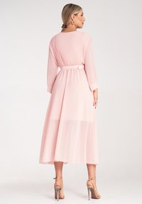 Długa, różowa sukienka z plisowanym tyłem, dopasowaną talią i zwiewną spódnicą z szyfonu. Posiada długie rękawy oraz pasek do związania w talii.