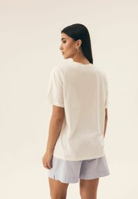 Biała koszulka z krótkim rękawem, okrągłym dekoltem, wykonana z miękkiego materiału. W połączeniu z jasnoniebieskimi spodniami w paski z bocznymi rozcięciami.