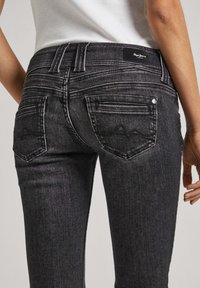 Czarne dżinsy z dopasowanym krojem, wyposażone w dwie tylne kieszenie oraz subtelny wzór na materiale. Metka widoczna na tylnej części w pasie.