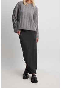 Grauer Kabelstrickpullover mit überschnittenen Schultern, kombiniert mit einem schwarzen Maxirock mit Nadelstreifen und klobigen schwarzen Schuhen mit Hardware-Details.