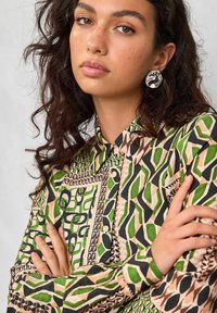Camisa de cuello con un patrón geométrico en colores verde, negro y durazno; la textura de la tela parece suave con detalles de botones.