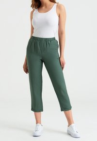 Gröna, korta byxor med elastisk midja och sidofickor, gjorda av lätt tyg; kombinerat med en vit tanktopp och vita sneakers.