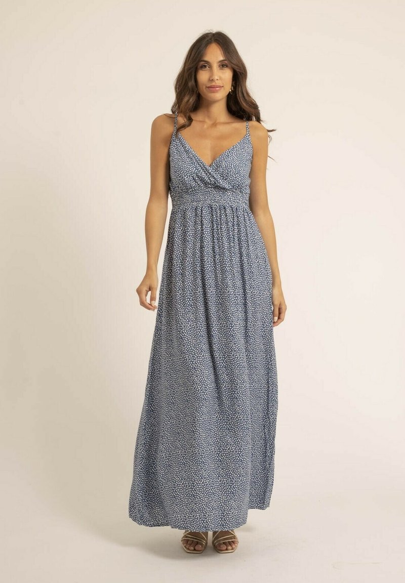 Robe maxi bleue à pois blancs, présentant un corsage drapé, des bretelles fines et une jupe fluide et texturée jusqu'à la cheville.