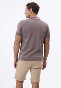Polo shirt pour homme à manches courtes en brun doux, en mélange de coton avec une finition texturée et un col étroit, associé à un short de couleur claire.