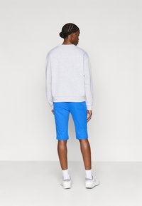 Grå hettegenser med rund hals, sammen med blå shorts som når midt på låret. Hvit sneakers fullfører antrekket. Rent, minimalistisk design.