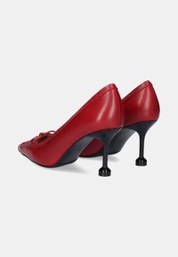 Zapatos de tacón alto de cuero rojo con punta afilada y tacón de aguja negro, con un borde festoneado y un detalle de costura decorativa.