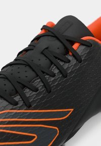 Chaussures de sport noires avec dessus texturé, accents orange, lacets noirs et capot de protection lisse. Présente un détail de logo sur le côté.