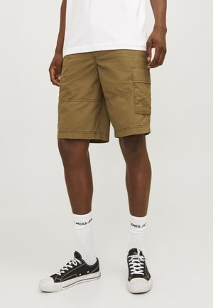 Khaki cargoshorts med flera fickor och sömdekorationer, tillverkade av lätt tyg. Kombination med svarta sneakers och vita strumpor.