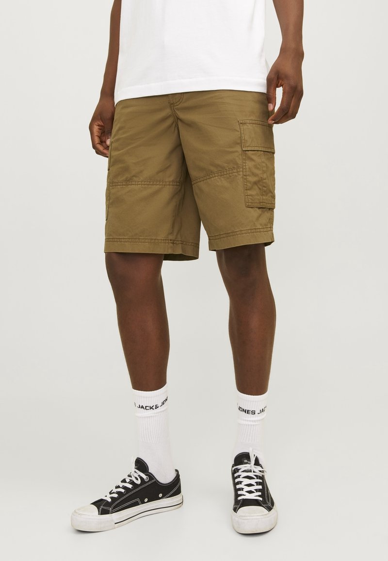 Khaki cargoshorts med flera fickor och sömdekorationer, tillverkade av lätt tyg. Kombination med svarta sneakers och vita strumpor.
