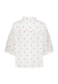 White short-sleeve shirt with a collared neckline, featuring a pattern of small red hearts. Textured, lightweight fabric with a relaxed fit.