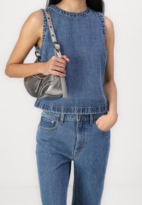 Top azul de mezclilla sin mangas con cuello redondo, dobladillo deshilachado y jeans de tiro alto a juego. Sostiene un pequeño bolso de cuero plateado.