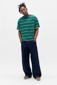 Grün gestreiftes T-Shirt mit kurzen Ärmeln und Rundhalsausschnitt, kombiniert mit lockeren, dunkelblauen Jeans und beigen Schuhen.