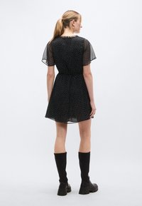 Μαύρο φόρεμα με κοντά, διαφανή μανίκια, με εφαρμοστή μέση και σχέδιο πουά. Συνδυασμένο με μαύρες μπότες μέχρι το γόνατο.