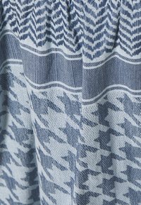 Tela tejida que presenta patrones de boca de perro y chevron en azul marino oscuro y azul claro, con un acabado texturizado y un borde superior elástico.