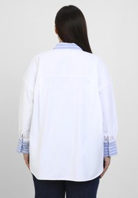 White shirt with a blue striped collar and cuffs, loose fit, long sleeves, and smooth texture. Back view highlights the clean design.