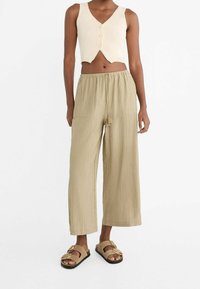 Top court côtelé crème avec un col en V et des détails de boutons, associé à un pantalon beige ample et froissé avec des poches latérales. Sandales tan.