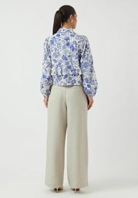 Blus med blommönster i vit och blått med puffärmar, matchad med ljusbeige vida byxor. Slät textur och skräddarsydd passform.