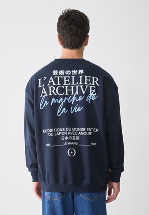 Sudadera de color azul marino hecha de algodón, con gran texto en blanco y azul claro en la parte posterior, de mangas largas y un ajuste relajado.