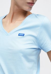 Ανοιχτό γαλάζιο T-shirt με V λαιμόκοψη κατασκευασμένο από απαλό ύφασμα, με ένα μικρό μπλε σημάδι λογότυπο "HUGO" στην αριστερή περιοχή του στήθους.
