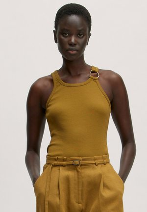 Gestreepte mosterdkleurige tanktop met één schouderband en een zilveren ringdetail, gecombineerd met bijpassende hoog getailleerde broek en een riem.