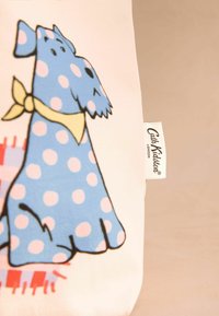 Blaue Polka-Dot-Hund-Illustration mit einem gelben Halstuch auf einem cremefarbenen Hintergrund. Weißes Etikett mit der Aufschrift "Cath Kidston London" sichtbar.