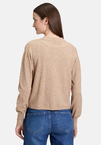 Beiger Pullover mit entspannter Passform, gerippten Bündchen und kleinem Kragen. Kombiniert mit blauen Denim-Jean für einen lässigen, schichtigen Look.