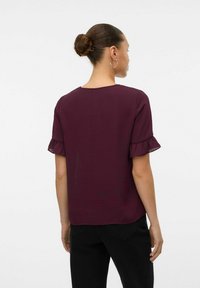 Bordeaux korteblouw met ruffle manchetjes, lichtgewicht stof, ronde halslijn en een gladde textuur, gedragen met zwarte broek.