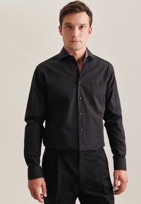 Schwarzes Langarmhemd mit aufknöpfbarer Front, einer einzelnen Brusttasche und kontrastierendem Kragen. Hergestellt aus glattem, leichtem Stoff.