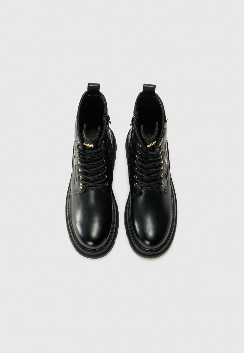 Zwarte leren enkellaarzen met metalen oogjes, ronde neus en platte zool. Voorzien van zwarte veters en decoratieve gouden hardware accenten.