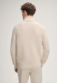 Beiger Strickpullover mit hohem Kragen, gerippten Bündchen und Saum. Verfügt über ein strukturiertes Muster und eine lockere Passform. Geeignet für kühlere Wetter.