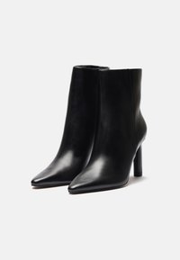 Bottines en cuir noir à bout pointu et à talon haut élancé. Texture lisse avec un design épuré et sans éléments visibles.