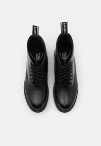 Botas de tobillo de cuero negro con una superficie lisa, puntera redonda, cordones en la parte delantera y tiradores con texto en contraste en la parte posterior.