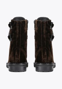 Brown suede ankle boots with black studded hardware, featuring two decorative buckles and a textured finish, positioned with a flat sole.