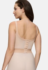 Donna che indossa un capo modellante beige nudo con chiusura posteriore e spalline regolabili, mostrata di spalle su uno sfondo neutro.