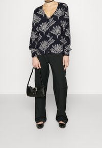 Blusa blu navy con bottoni, caratterizzata da un motivo di foglie bianche, abbinata a pantaloni neri a gamba larga e una piccola borsa nera. Tessuto morbido, vestibilità rilassata.