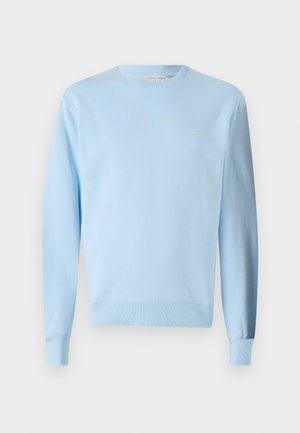 Svetlo modrý bavlnený sveter s dlhými rukávmi, rebrovanými manžetami a spodným lemom. Obsahuje malú vyšívanú značku v jemnom zlatom odtieni.