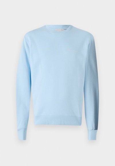 Ανοιχτό μπλε βαμβακερό φούτερ με μακριά μανίκια, ραμμένα μανίκια και στρίφωμα. Έχει ένα μικρό κεντητό λογότυπο σε διακριτική χρυσή απόχρωση.