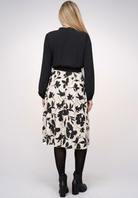 Maglietta nera a maniche lunghe abbinata a una gonna color crema con un motivo floreale nero. Stivali neri alla caviglia completano l'outfit.
