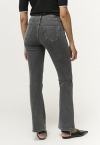 Jeans de mezclilla gris acampanados con una cintura de talle medio, que cuentan con dos bolsillos traseros y costuras visibles, combinados con zapatos negros tipo slip-on.
