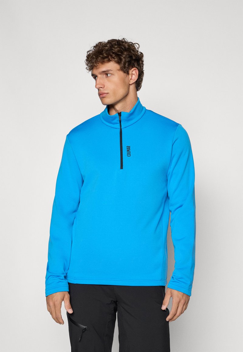 Ανοιχτού μπλε αθλητικό πουλόβερ με ψηλό γιακά, μισό φερμουάρ και μαύρη λεπτομέρεια λογότυπου. Φτιαγμένο από λείο, ελαστικό ύφασμα για άνεση.