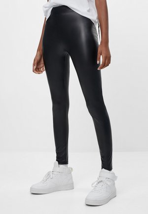 Leggings neri, elasticizzati con una finitura lucida e vita alta, abbinati a sneakers bianche alte. Adatti per un look casual.