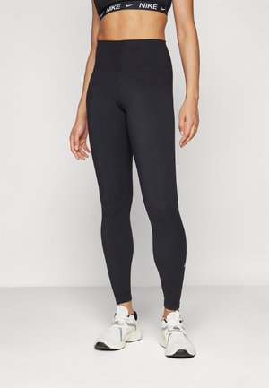 Svarte høytliv leggings laget av elastisk materiale. Har en glatt overflate og en subtil Nike-logo ved ankelen. Kombinert med hvite joggesko.