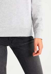 Felpa grigia dalla texture liscia e collo tondo, abbinata a jeans neri con finitura leggermente slavata e tasche anteriori.